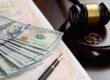 Divorce settlement concept with judge’s gavel, wedding rings, cash, and legal documents on desk.