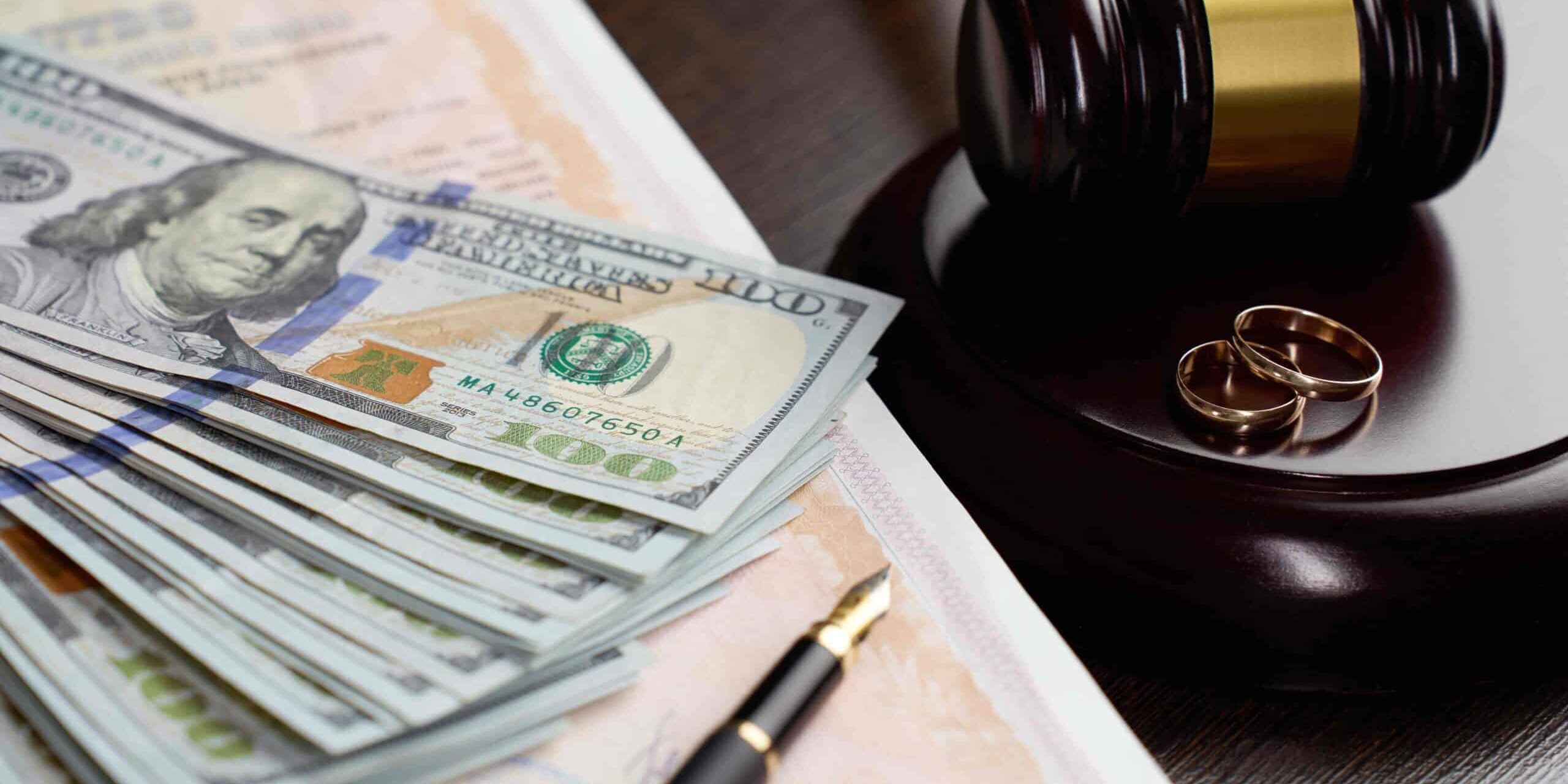 Divorce settlement concept with judge’s gavel, wedding rings, cash, and legal documents on desk. Divorce settlement concept with judge’s gavel, wedding rings, cash, and legal documents on desk.
