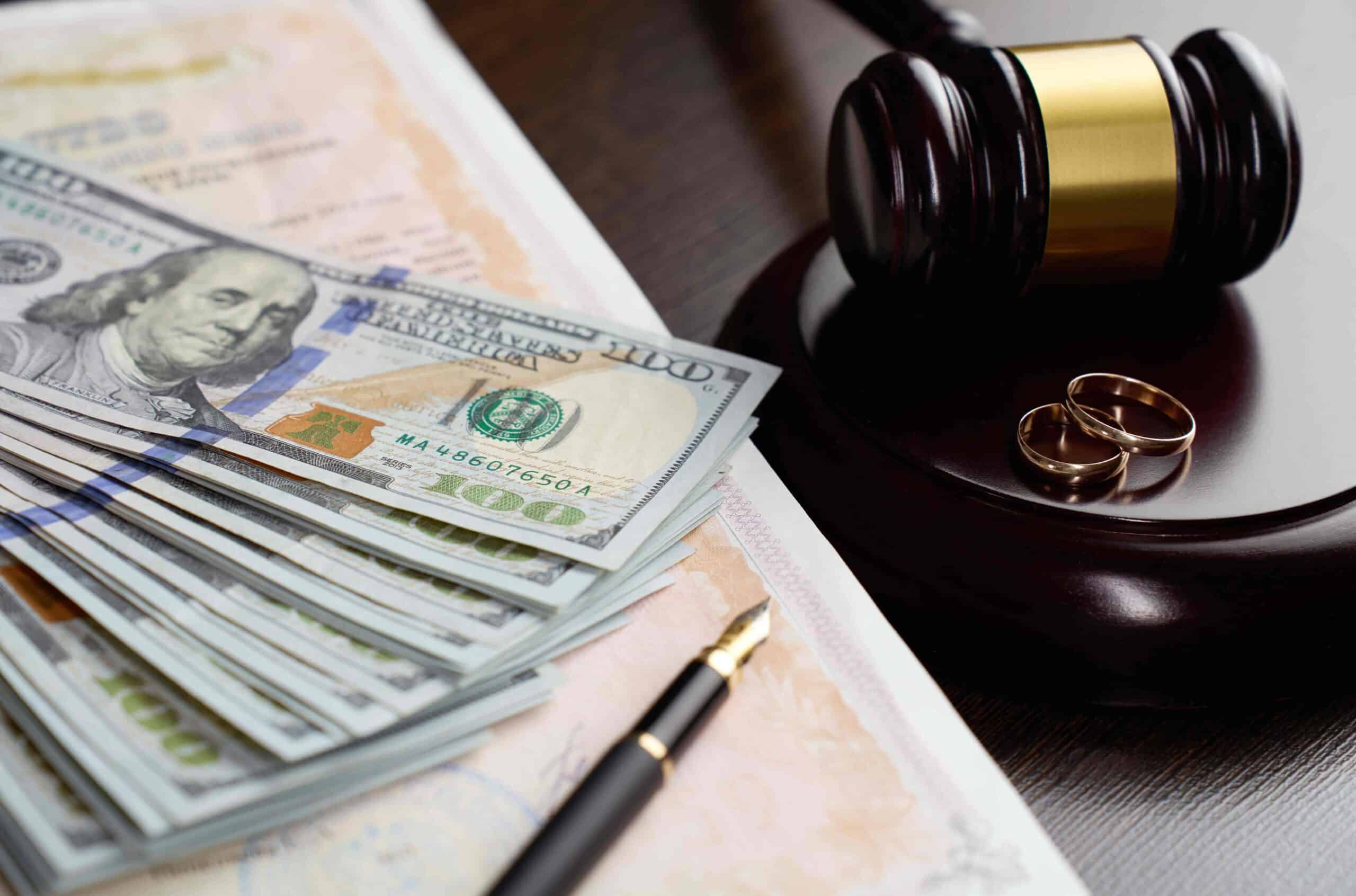 Divorce settlement concept with judge’s gavel, wedding rings, cash, and legal documents on desk. Divorce settlement concept with judge’s gavel, wedding rings, cash, and legal documents on desk.