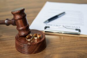 Divorce decree, gavel and rings on warm wooden surface