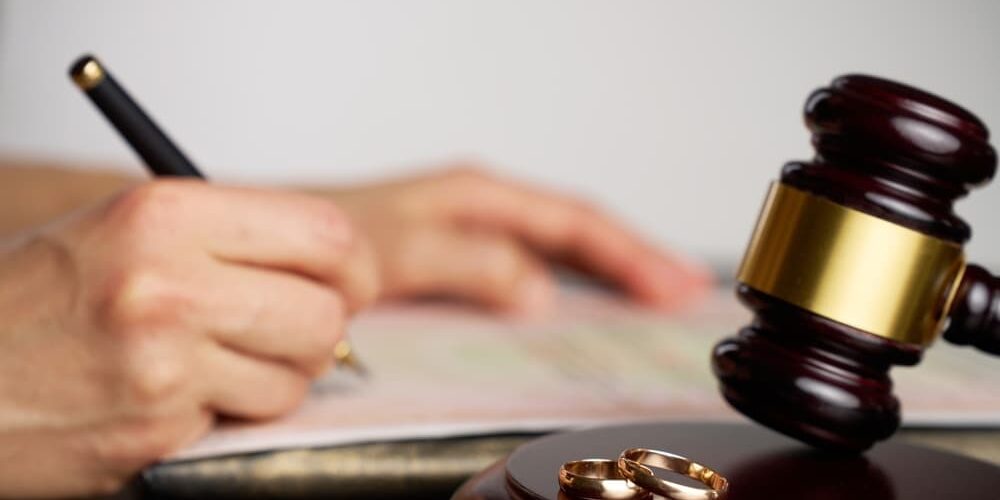 What Are the Grounds for Divorce in Michigan Close-up of a person signing divorce document, with a judge gavel and wedding rings in focus.