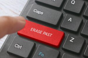 Selective focus of a finger and a red button computer keyboard written with Erase Past. 