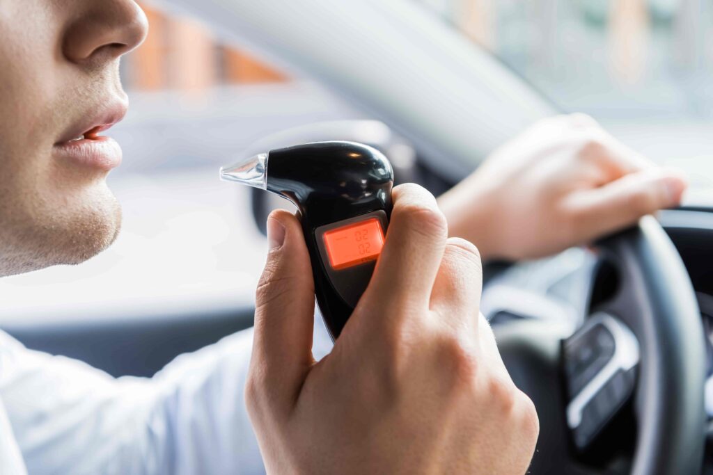 Driver using breathalyzer device to check blood alcohol level before driving.