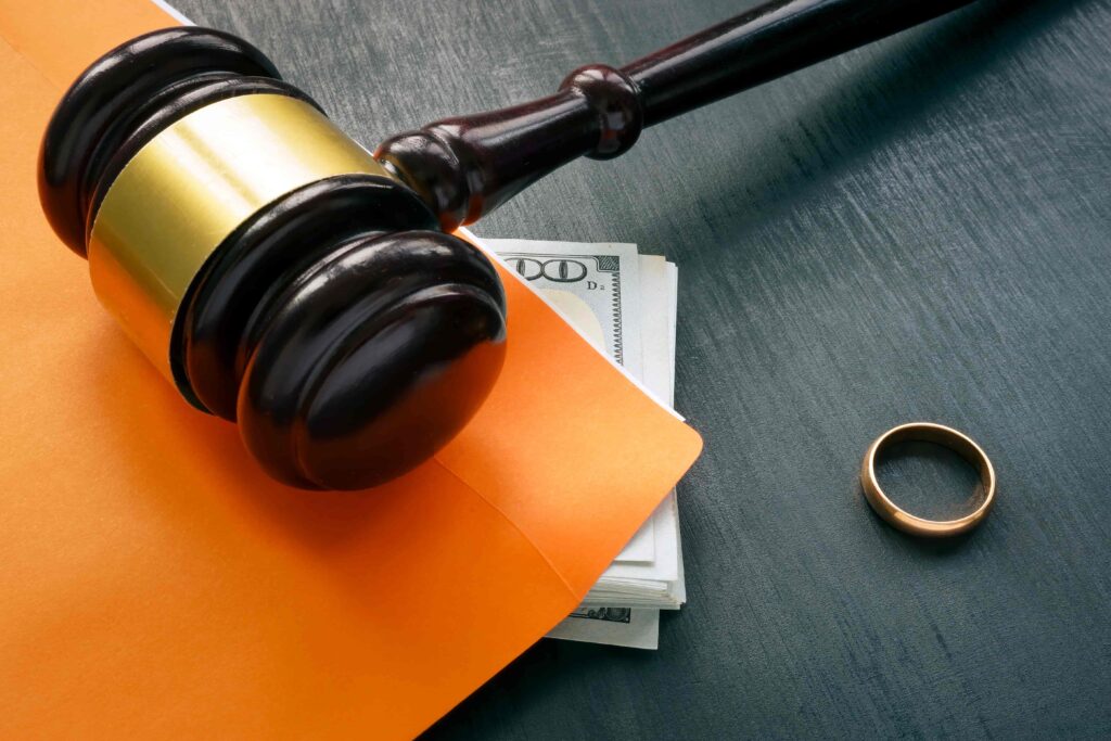 Judge’s gavel with money, legal documents, and wedding ring symbolizing divorce settlement or alimony case.