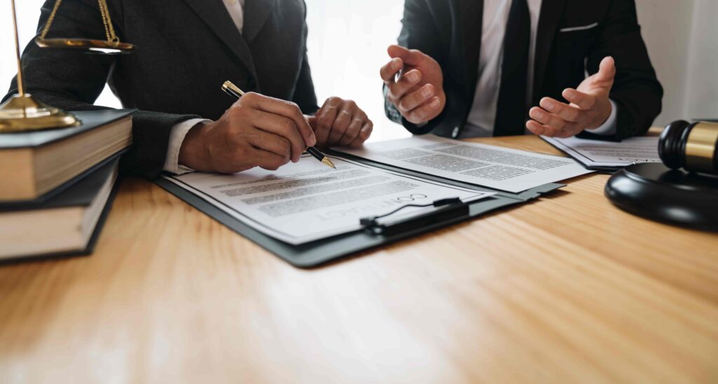 Lawyer reviewing legal contract with client in office, discussing agreement details with documents and gavel on desk.