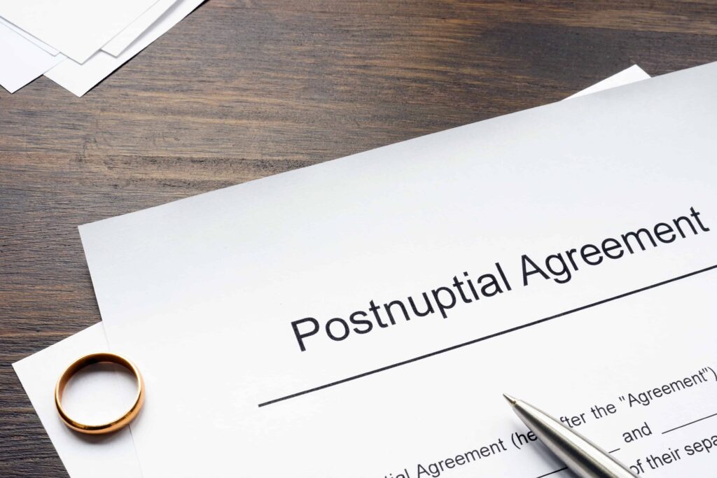 Postnuptial agreement document with wedding ring and pen on wooden desk.